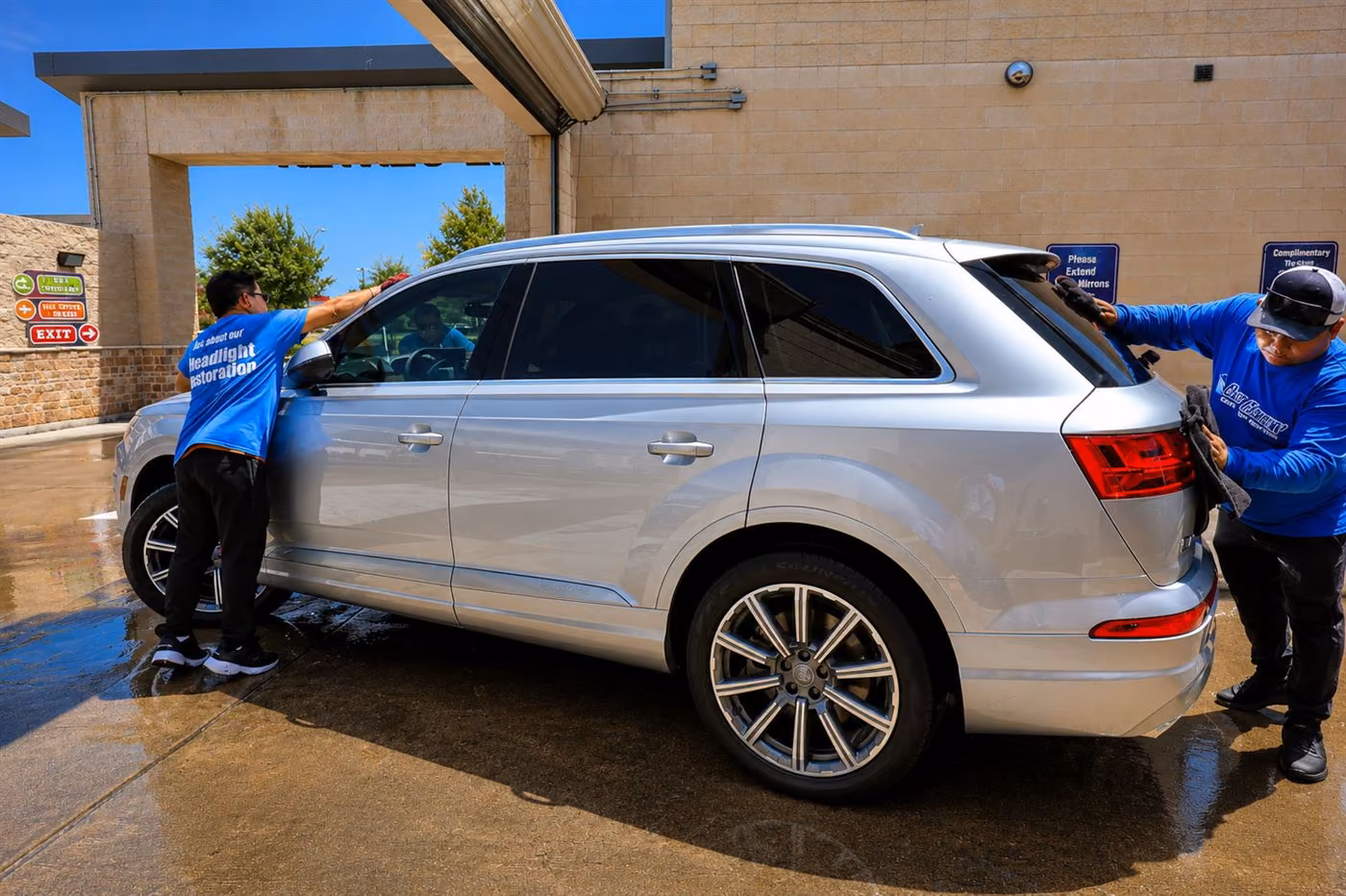 Two crew members hand-drying a silver SUV under the canopy