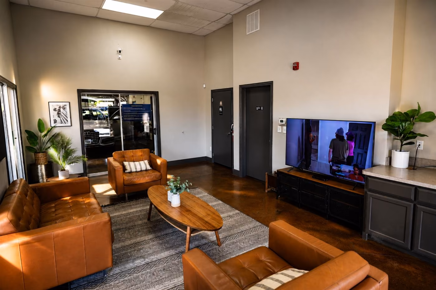 Quiet Detail Center lounge with tan leather chairs, a coffee table, plants, and a wall-mounted TV