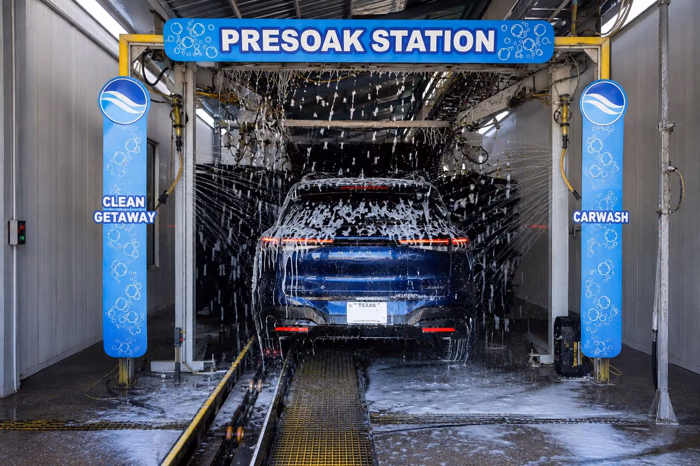 Dark SUV covered in foam inside the wash tunnel under the Presoak Station sign