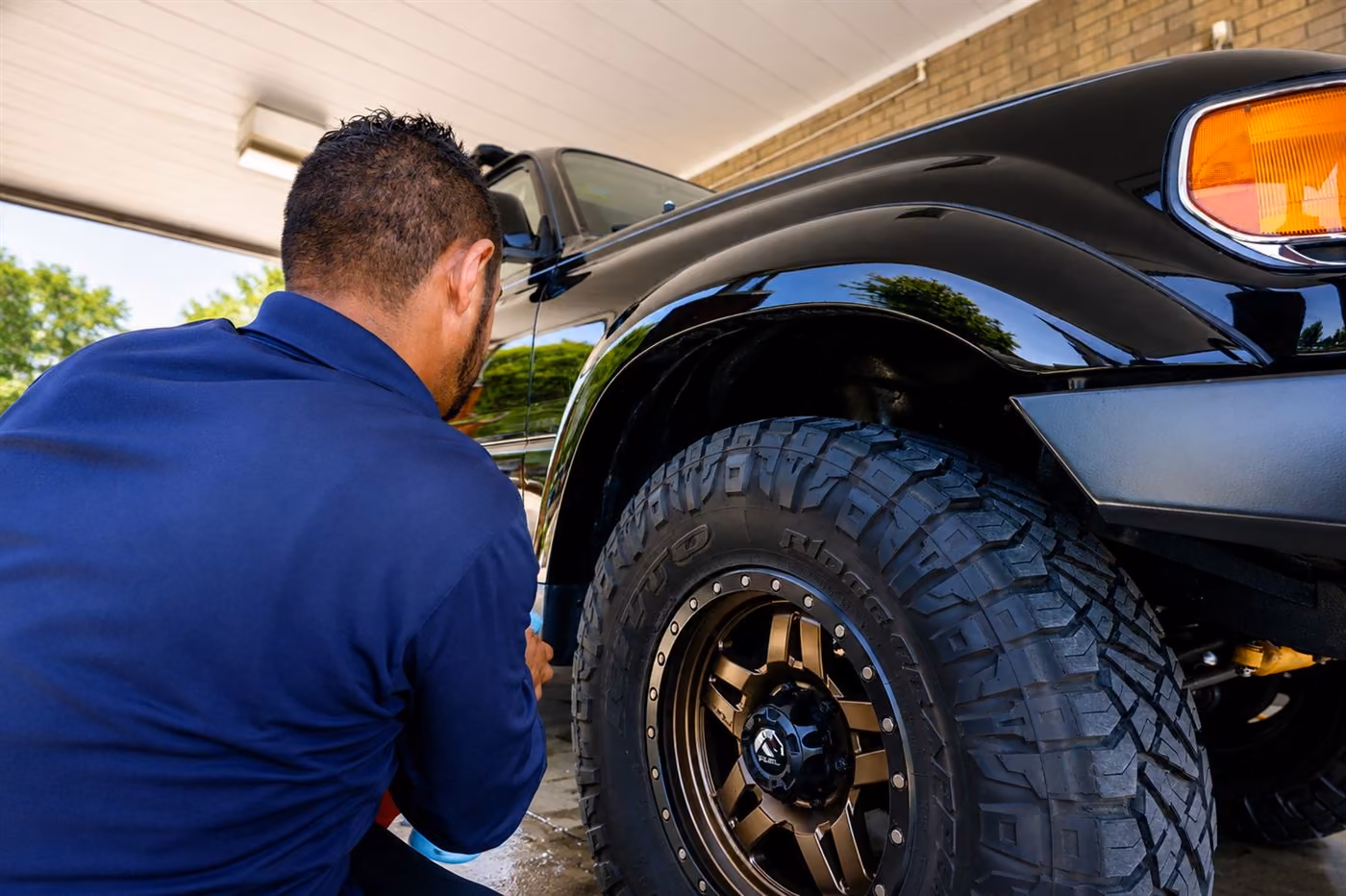 Detailer hand-cleaning the wheel and tire of a lifted black truck